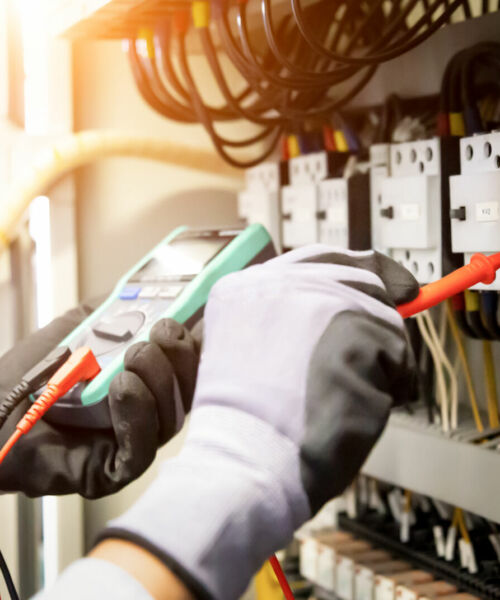 Engenheiro eletricista utilizando multímetro digital para medição de tensão em painel elétrico industrial