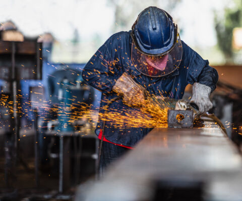 Worker using electric wheel grinding on steel structure in factory.